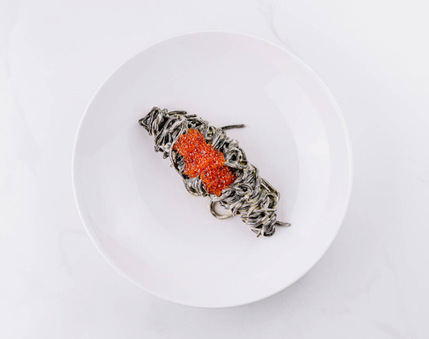Элегантная презентация пасты из чернил кальмара с роскошной красной икрой на белой тарелке - Фото, изображение