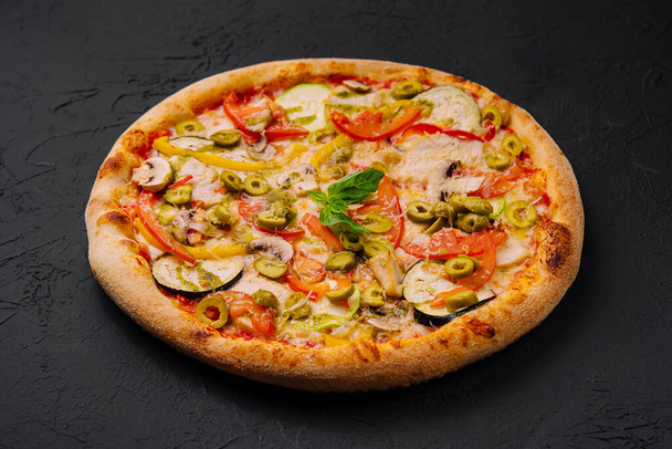 Lebendige Gemüsepizza mit verschiedenen Belägen auf dunkler, strukturierter Oberfläche - Foto, Bild