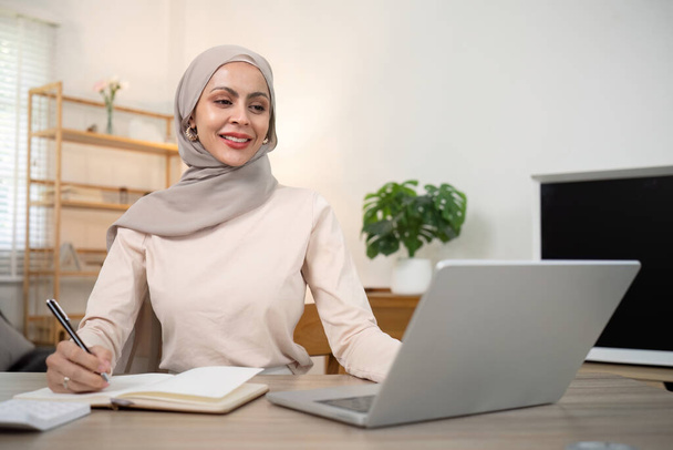 Joven mujer musulmana contable de negocios que trabaja con facturas de documentos financieros, calcular impuestos. Mujer musulmana freelancer papeleo en casa. - Foto, imagen