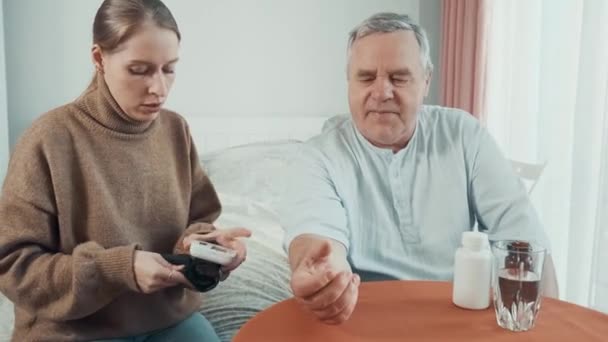 Pečující dospělá dcera měří krevní tlak na svém starém otci doma na zápěstí. Mladá žena kontroluje puls dospělého muže zdravotnickým zařízením. Rodinná péče a Den otců koncept. - Záběry, video