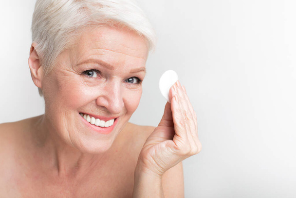 Anciana europea presenta una almohadilla de algodón mientras sonríe, reflejando higiene y momentos alegres de s3niorlife - Foto, Imagen