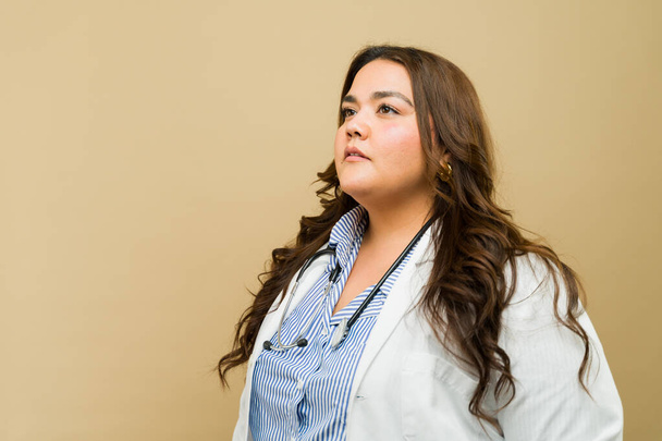 Doctora hispana con sobrepeso se levanta orgullosamente en un estudio, exudando confianza y gracia - Foto, imagen