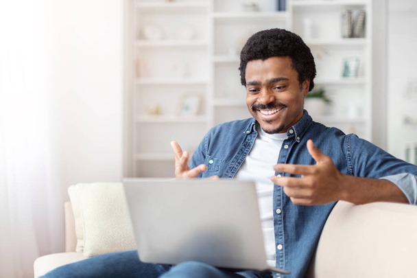 Un ragazzo afroamericano nero viene visto ridere gioiosamente durante una videochiamata a casa, interagendo con un uomo sul suo computer portatile. - Foto, immagini