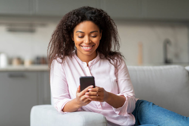 Uma senhora afro-americana é visto confortavelmente mensagens de texto em seu smartphone, proporcionando um vislumbre da vida doméstica e hábitos milenares - Foto, Imagem