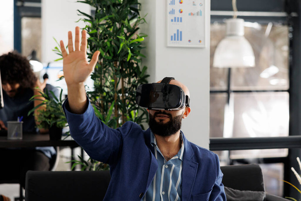 Businessman in virtual reality headset working in start up business office. Company employee exploring metaverse and brainstorming in vr glasses in corporate coworking space - Photo, Image