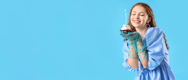 Όμορφη ευτυχισμένη νεαρή γυναίκα κρατώντας cupcake γενεθλίων σε γαλάζιο φόντο με χώρο για κείμενο - Φωτογραφία, εικόνα
