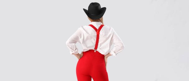 Mujer joven con estilo en pantalones rojos y con tirantes sobre fondo claro, vista trasera - Foto, Imagen