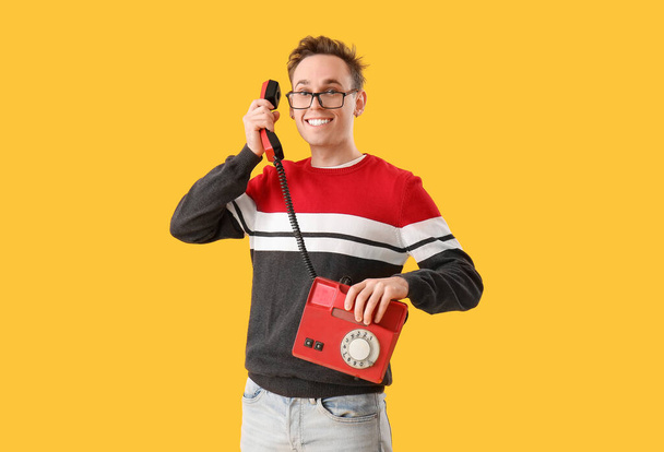 Happy young man with telephone on yellow background - Фото, зображення
