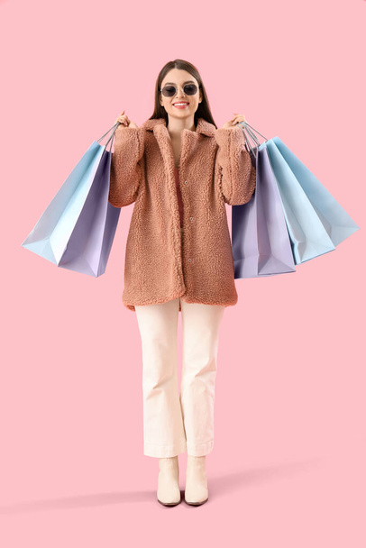 Νεαρή γυναίκα με τσάντες για ψώνια σε ροζ φόντο - Φωτογραφία, εικόνα