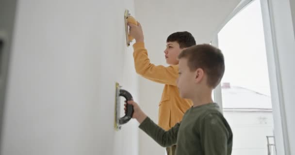 Twee jonge jongens die deelnemen aan een familie renovatie project, gladstrijken muur oppervlakken in hun nieuwe huis. Dit moment vangt de essentie van teamwork en de vreugde van het creëren van een leefruimte samen - Video