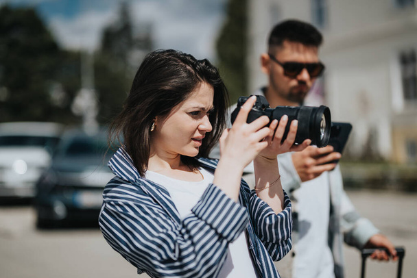 Eine fokussierte junge Frau benutzt eine professionelle Kamera in einem städtischen Umfeld, geführt von einem männlichen Kollegen. - Foto, Bild