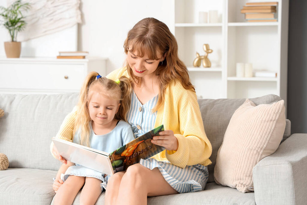 Nanny reading story to little girl on sofa at home - Photo, Image