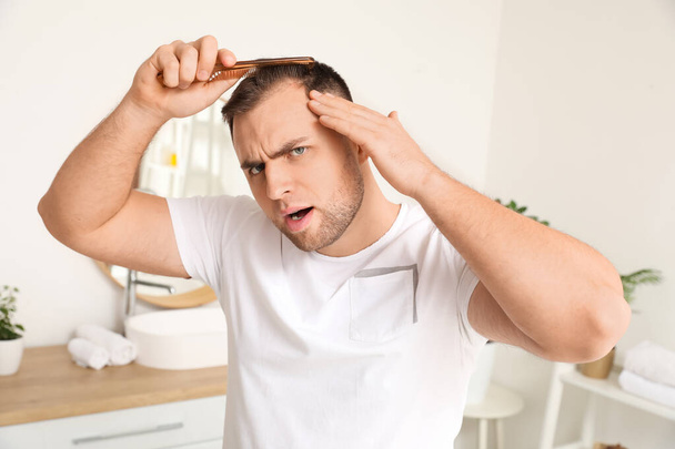 Беспокойный молодой человек с проблемой выпадения волос расчесывание в ванной комнате - Фото, изображение