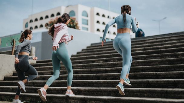 Aktywne młode kobiety w stroju treningowym ćwiczące razem biegając po schodach miejskich, pokazując zdrowie i towarzystwo. - Zdjęcie, obraz