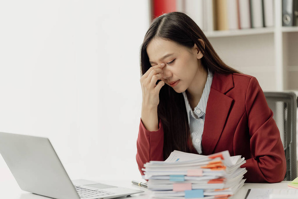 Aziatische vrouwelijke accountant lijdt aan oogspanning van staren naar een scherm voor een lange tijd, stress en hoofdpijn. Er is een probleem met haar project. Bezorgd over haar zakelijke financiën - Foto, afbeelding