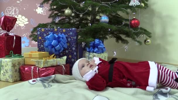 Mooie babymeisje liggen in de buurt van de kerstboom en huidige geschenkverpakkingen - Video