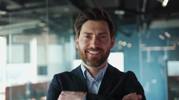 Close-up van positieve Kaukasische man glimlachend op grote schaal, terwijl hij staat tegen doorschijnende uitgestrektheid van de kantoormuur. Aantrekkelijke zakenman in donker formeel pak met vastberadenheid op de werkplek. - Video