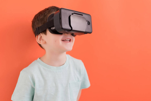 Kaukasischer Junge mit Virtual-Reality-Headset-Brille auf orangefarbenem Hintergrund mit Kopierraum - Foto, Bild