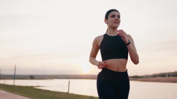 Młoda kobieta w odzieży sportowej biegnie wzdłuż wału o zachodzie słońca. Koncepcja zdrowego stylu życia - Materiał filmowy, wideo