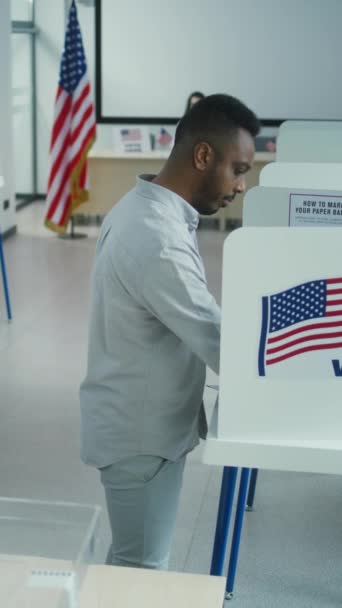 Homem afro-americano vota para candidato presidencial em cabine de votação na estação de votação, em seguida, coloca cédula de papel na caixa. Cidadão americano masculino durante o Dia das Eleições Nacionais nos Estados Unidos. Direito cívico. - Filmagem, Vídeo