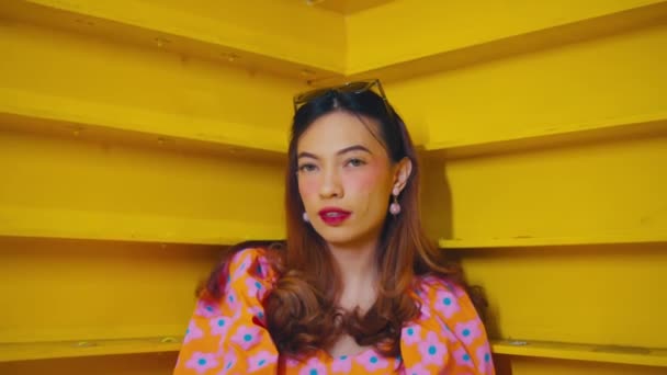 Stylish woman in floral dress posing against yellow staircase, exuding confidence and retro fashion vibes during the daylight - Footage, Video