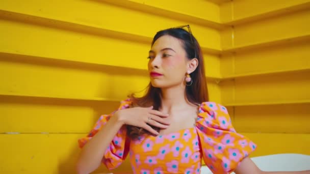 Стильна жінка в квітковому платті позує на яскраво-жовтих сходах, виключаючи впевненість і літо вібрує під час денного світла - Кадри, відео