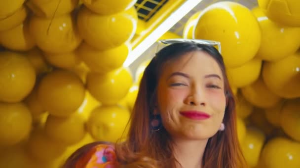Kobieta uśmiechnięta w pokoju wypełnionym żółtymi kulkami w dzień - Materiał filmowy, wideo