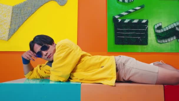 a man with sunglasses is relaxing on a brightly colored box in a very vibrant room in the day - Кадры, видео