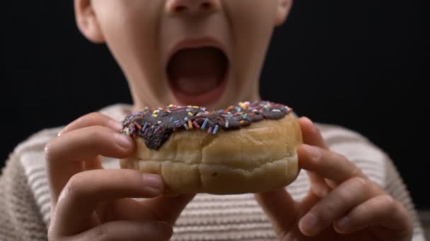 Kind hält Donut in der Hand, wartet geduldig auf Zuckerrausch und konzentriert sich mit offenem Mund auf süße Leckereien. Verzögertes Befriedungskonzept - Filmmaterial, Video