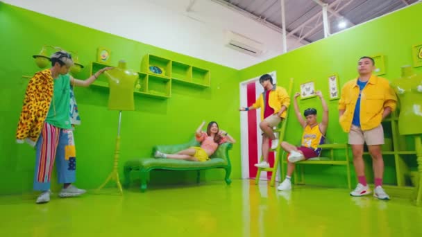 Skupina módních mladých lidí se baví v živé, barevné místnosti se zelenými stěnami, moderním nábytkem a hravými pózami za denního světla - Záběry, video