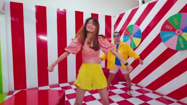 Movimento desfocado de duas pessoas dançando em uma sala vibrante e colorida com piso quadriculado e paredes listradas, transmitindo energia e diversão durante o dia - Filmagem, Vídeo