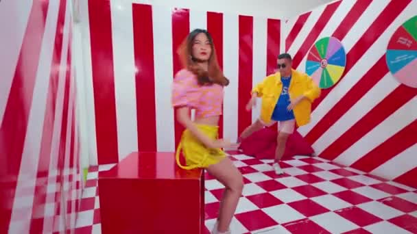 Kahden ihmisen hämärä liike tanssimassa elinvoimaisessa, värikkäässä huoneessa, jossa on ruudullinen lattia ja raidalliset seinät, jotka välittävät energiaa ja hauskaa päivänvalossa - Materiaali, video