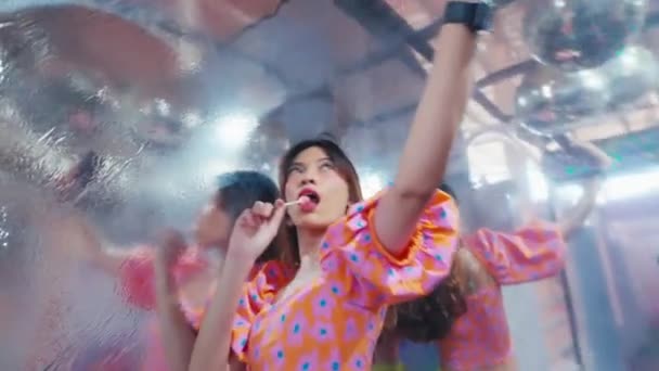 Молодая женщина делает селфи на яркой вечеринке с диско шаром и праздничными огнями в течение утра - Кадры, видео