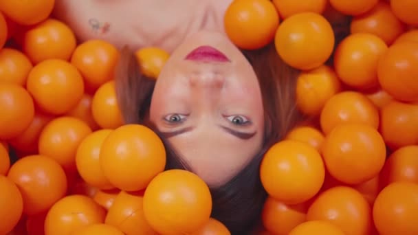 明るいオレンジ色のボールに囲まれた女性の顔は,朝の間に鮮やかで遊び心のあるイメージを作り出します - 映像、動画