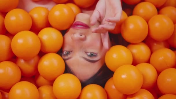Rosto de mulher cercado por bolas laranja, conceito brincalhão e colorido durante a manhã - Filmagem, Vídeo