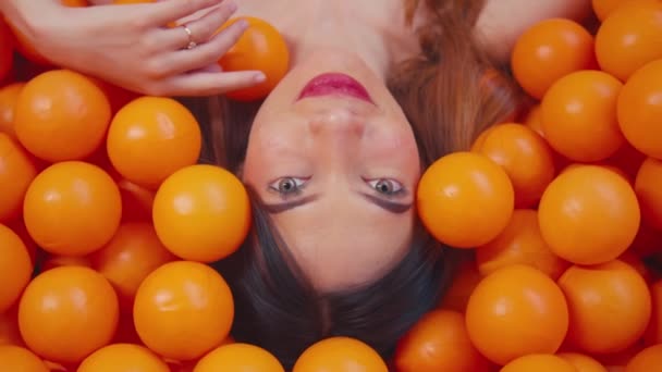 Vrouw liggend in een plas sinaasappels, close-up op het gezicht met een speelse uitdrukking overdag - Video
