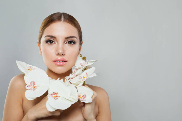 Wspaniała modelka z naturalnym makijażem, zdrową skórą i białym kwiatem. Kobieca uroda, kosmetyka i koncepcja pielęgnacji skóry - Zdjęcie, obraz