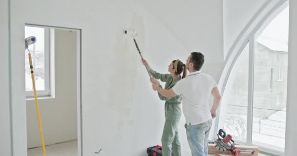 Pareja se involucra en un proyecto de renovación de casas, pintando las paredes interiores de su nuevo apartamento. Transformando su espacio vital con pintura. Esto captura un momento de trabajo en equipo y mejora doméstica - Imágenes, Vídeo