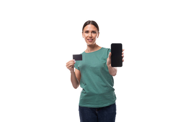 νεαρή μελαχρινή γυναίκα που κρατά μια πλαστική κάρτα με ένα mockup για έκπτωση και πίστωση και ένα smartphone. - Φωτογραφία, εικόνα