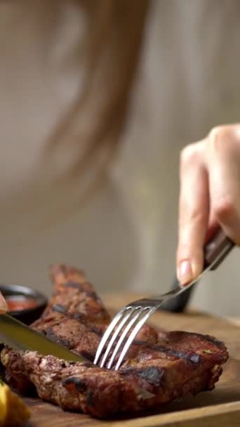 Primo piano di una donna che taglia una bistecca di maiale con un coltello mentre mangia carne in un ristorante. Video verticale - Filmati, video