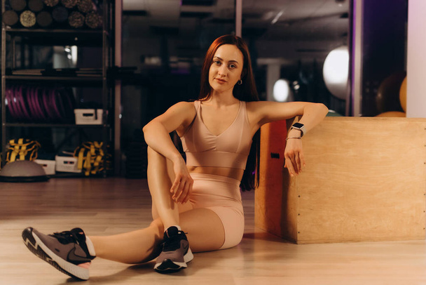 Una atleta se sienta en el gimnasio por la noche cerca de un cubo de madera - Foto, imagen