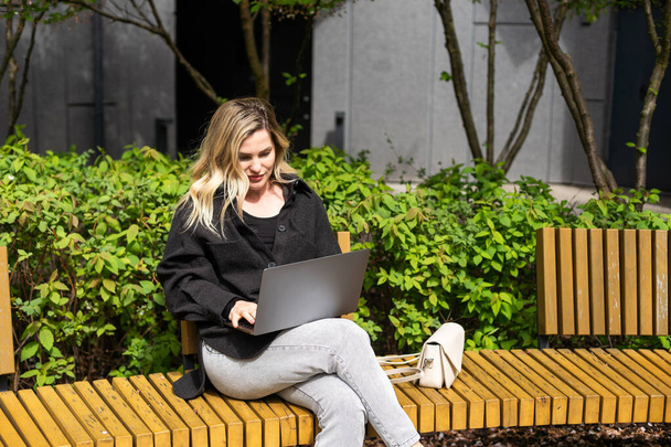 Mujer joven sentada en la reunión en línea en la cafetería al aire libre, hablando con la cámara portátil, explicando algo, beber café. Foto de alta calidad - Foto, imagen