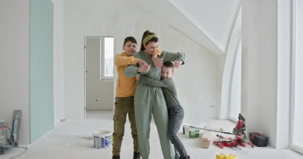 Een hartverwarmend tafereel van een gezin tijdens een woningrenovatie. Dit beeld vangt een moeder die haar twee zoons omarmt in een gedeeltelijk geschilderde ruimte, omringd door renovatietools en materialen. - Video