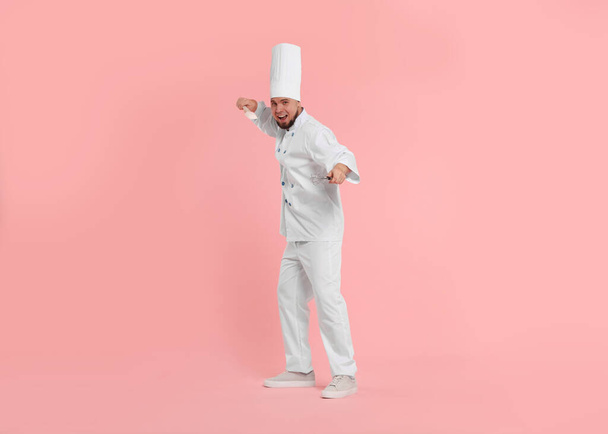 Happy professional confectioner in uniform holding spatula and whisk on pink background - Fotografie, Obrázek