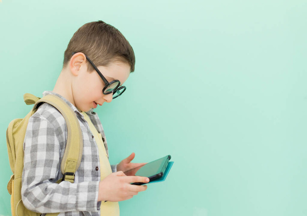 Blanke jongen in bril met schoolrugzak met tablet op een groene achtergrond met kopieerruimte - Foto, afbeelding