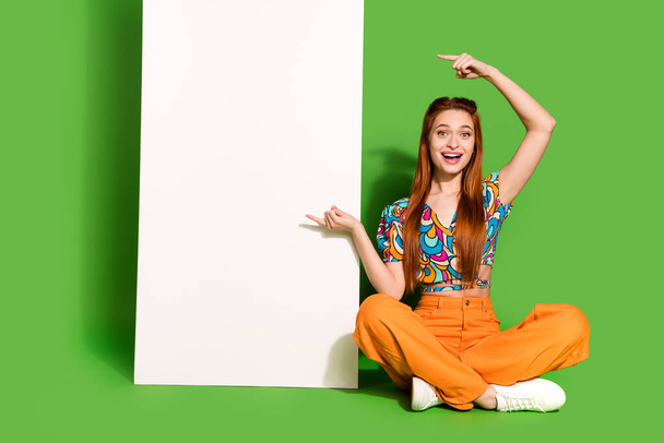 Full size photo of pretty young woman point fingers empty space placard wear top isolated on bright green color background. - Foto, immagini