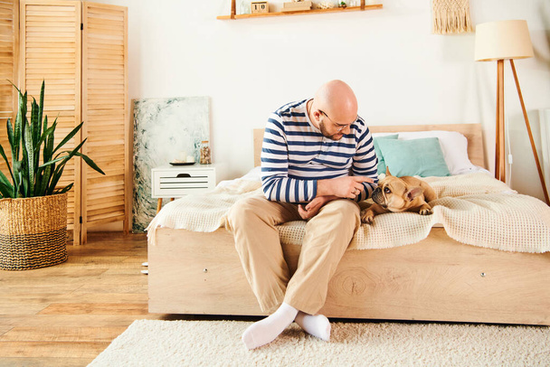Bonito homem sentado na cama, relaxando com fiel Bulldog francês. - Foto, Imagem