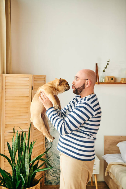 Een man omarmt liefdevol een Franse bulldog tegen zijn gezicht. - Foto, afbeelding