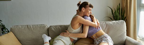 Zwei Frauen in kuscheliger Kleidung sitzen auf einer Couch und umarmen sich liebevoll. - Foto, Bild