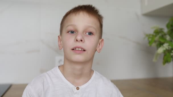 A young boy with striking blue eyes is captured looking upwards with a thoughtful expression in a brightly lit room adorned with a subtle indoor plant in the background, hinting at a serene home - Footage, Video
